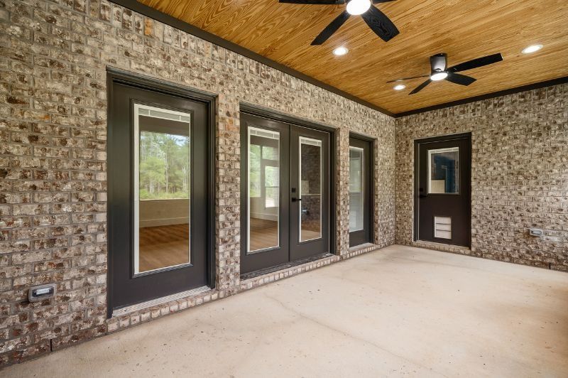 Brick-walled outdoor patio with dark doors and ceiling fans; tan floor and wood ceiling.