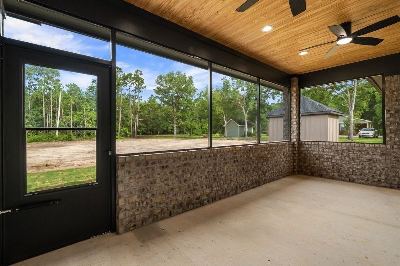 Screened porch with stone walls, concrete floor, and a wood ceiling overlooking a grassy area and trees.