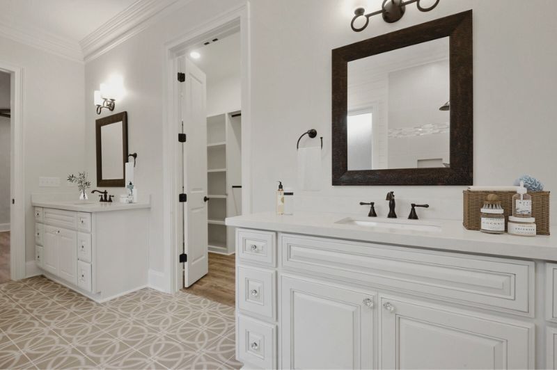 Bathroom with two white vanities, dark mirrors, and patterned floor.