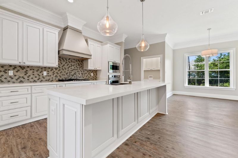 Bright, modern kitchen with white cabinets, island, and two pendant lights. Wooden floor and large window.