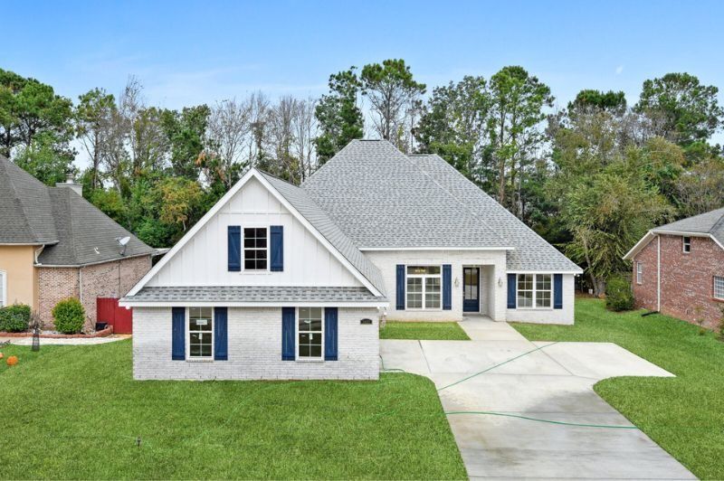 White brick house with gray roof, blue shutters, and green lawn.