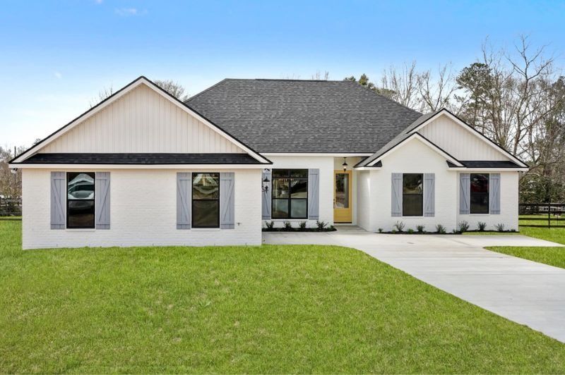 White brick house with gray shutters, a dark roof, and a green lawn.