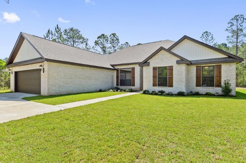 Tan brick ranch house with brown trim, a lawn, and trees.