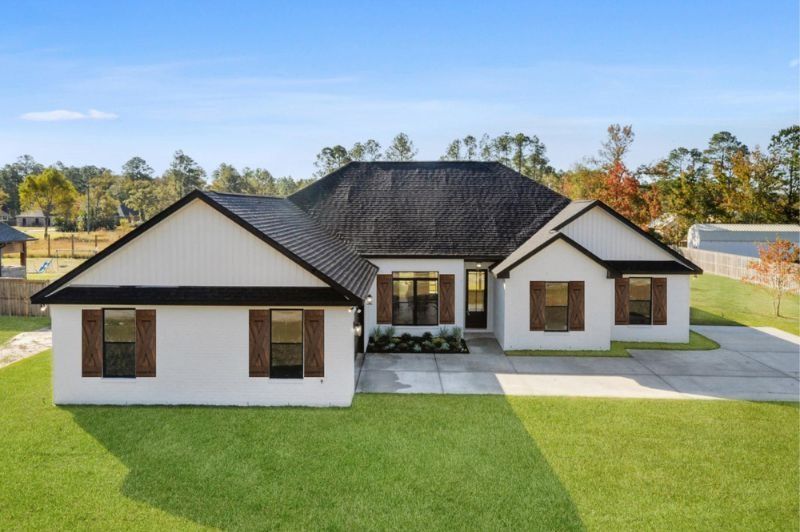 White house with black roof, brown shutters, and green lawn on a sunny day.