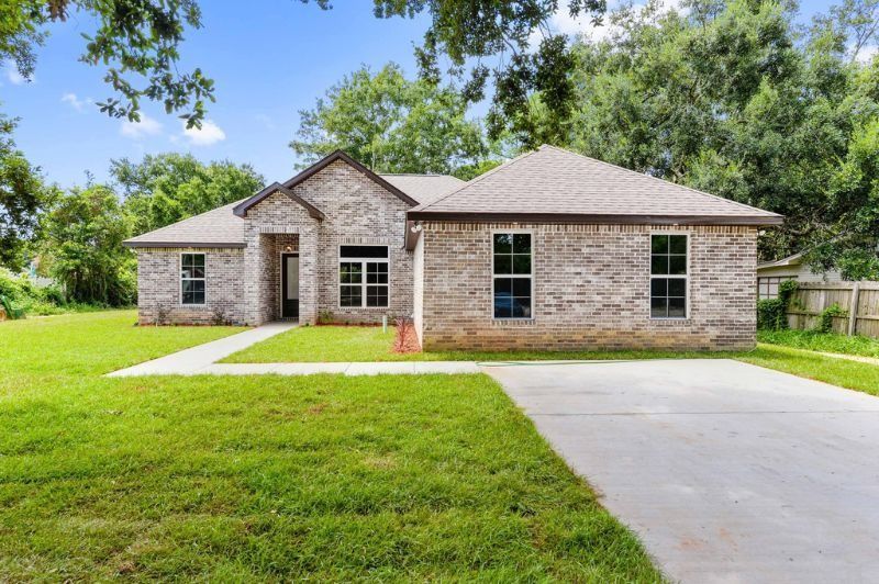 A single-story brick house with a concrete driveway and green lawn.