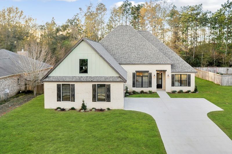 Cream-colored brick house with a gray roof and green trim, driveway, and green lawn.