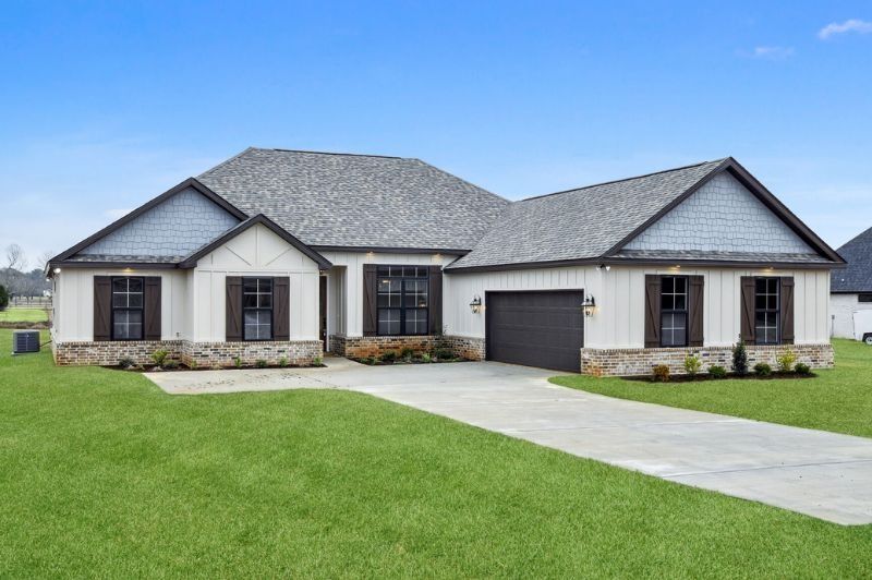 White and gray ranch-style house with dark shutters and a black garage door, situated on green grass.