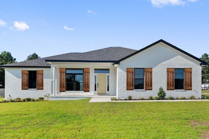 White brick house with black roof and brown shutters on a sunny day.