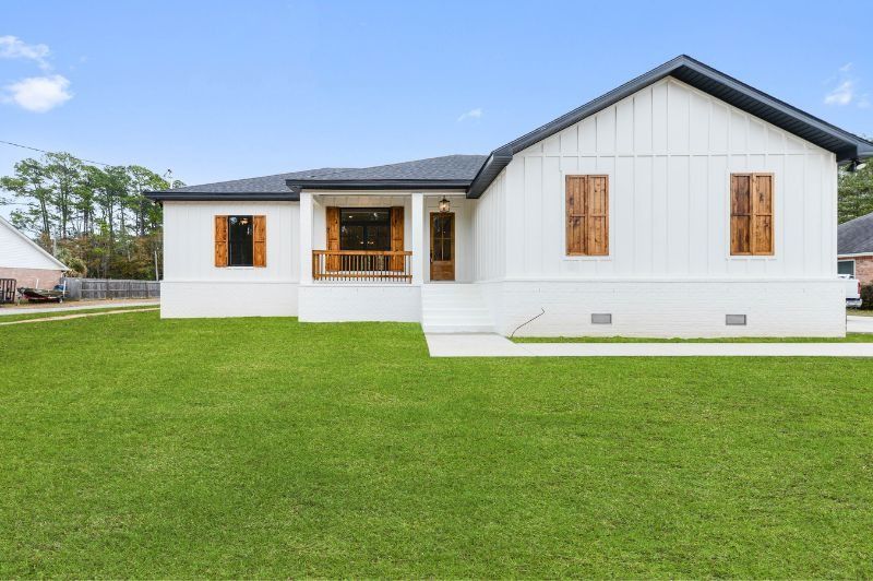 White modern farmhouse with brown shutters and porch, green lawn, blue sky.