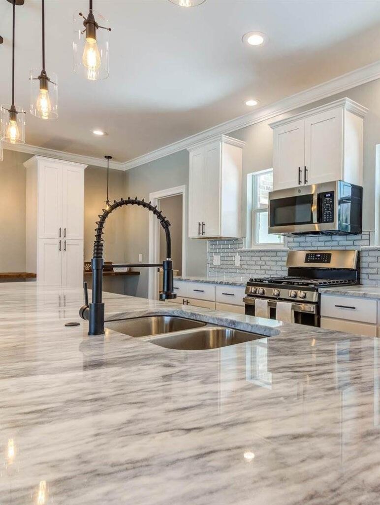 Modern kitchen with marble island, stainless steel appliances, and white cabinets.