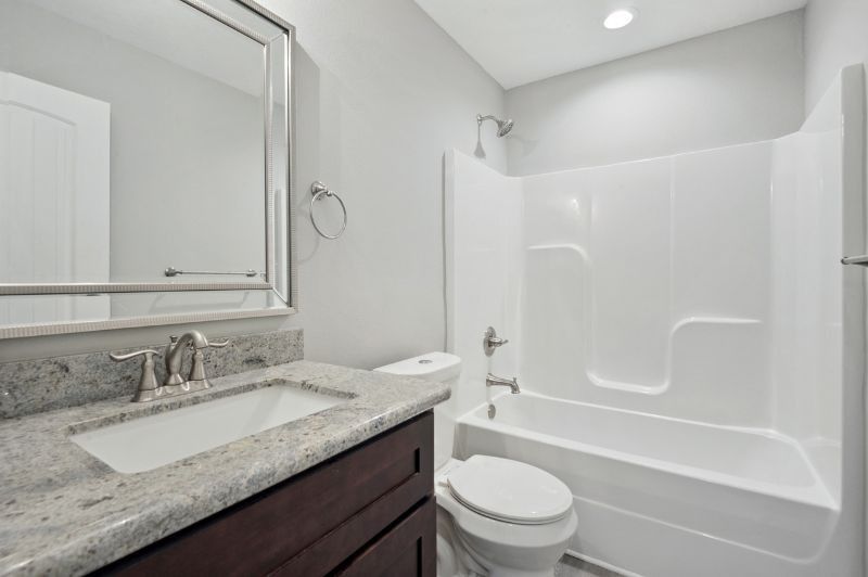 Bathroom with white tub and toilet, dark wood vanity, and gray walls.