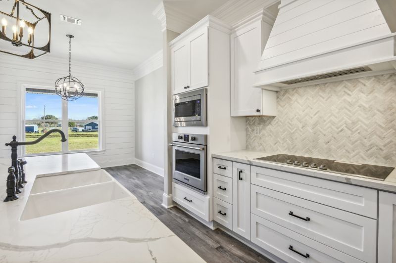 White kitchen with cabinetry, sink, appliances, and window overlooking a yard.