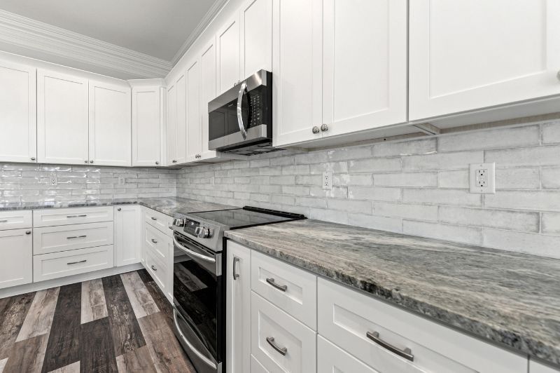 White kitchen with gray countertops, subway tile backsplash, and dark wood floor.
