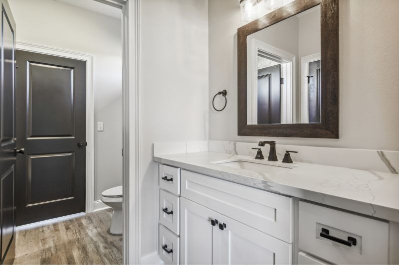 Bathroom with white vanity, marble countertop, dark fixtures, and a dark-framed mirror.