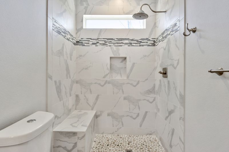 A modern shower with white marble tile, a small seat, and a recessed niche.
