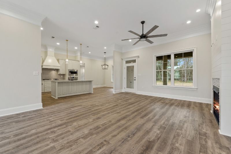 Open-concept living space with kitchen. Light wood floors, white walls, and a ceiling fan.