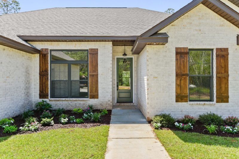White brick house with dark shutters and trim, walkway to glass door, and landscaping.
