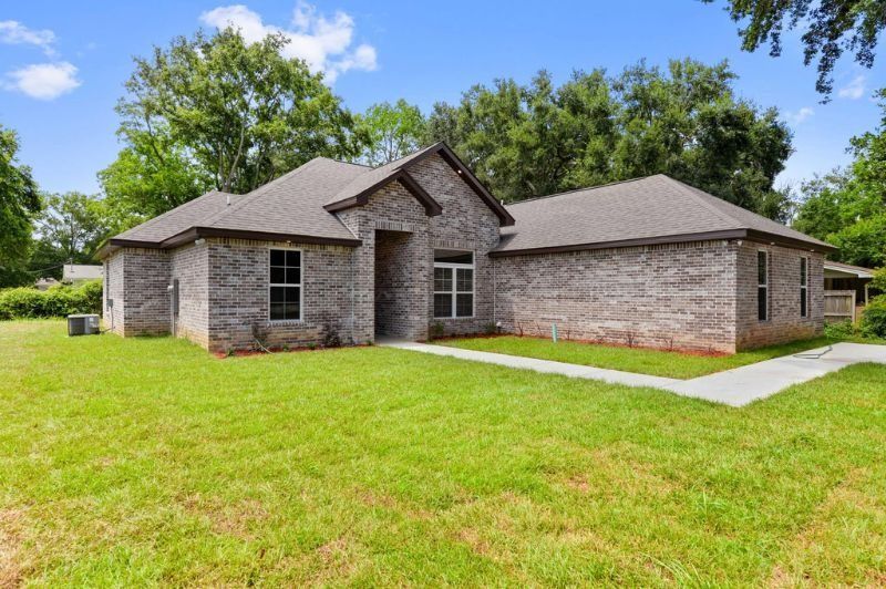 Brick house with green lawn and trees in the background on a sunny day.