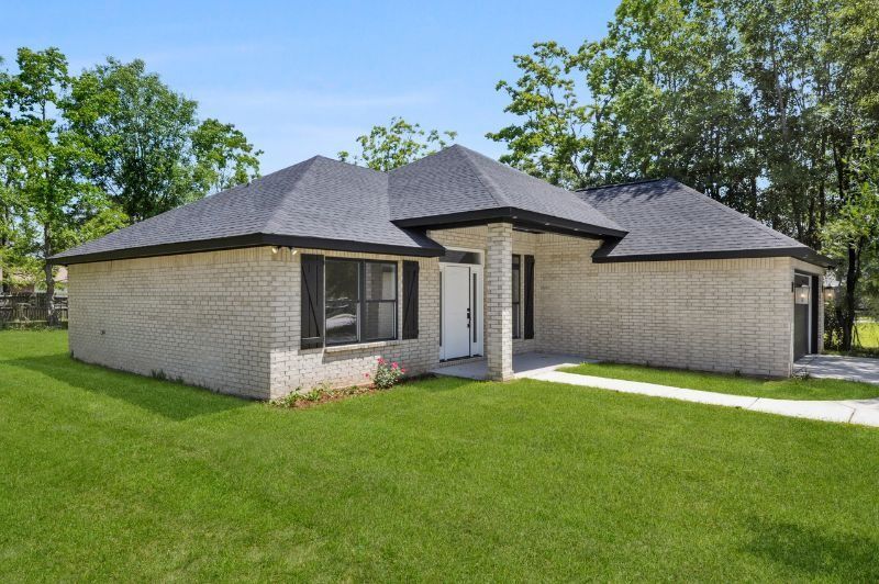 A one-story light brick house with a black roof and shutters, set on green grass.