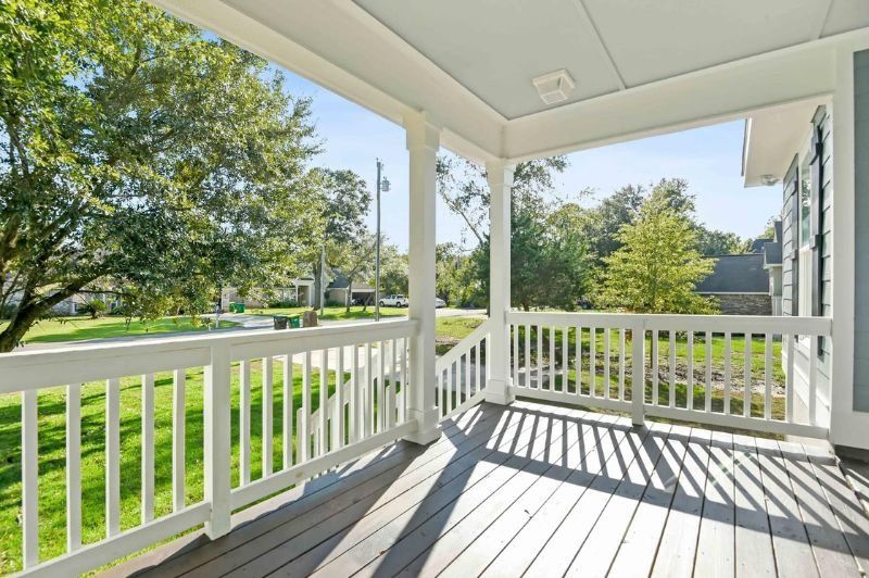 White porch with railing, overlooking a green lawn, trees, and street under a blue sky.