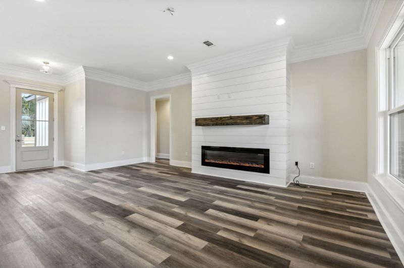 Empty room with gray wood floors, white shiplap fireplace, and large window.