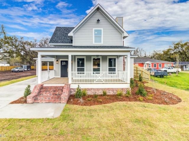 Gray two-story house with a front porch, brick steps, and a green lawn under a cloudy sky.