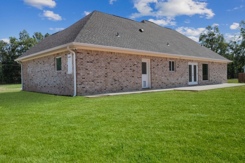 Brick house with dark gray roof, green grass, and blue sky.
