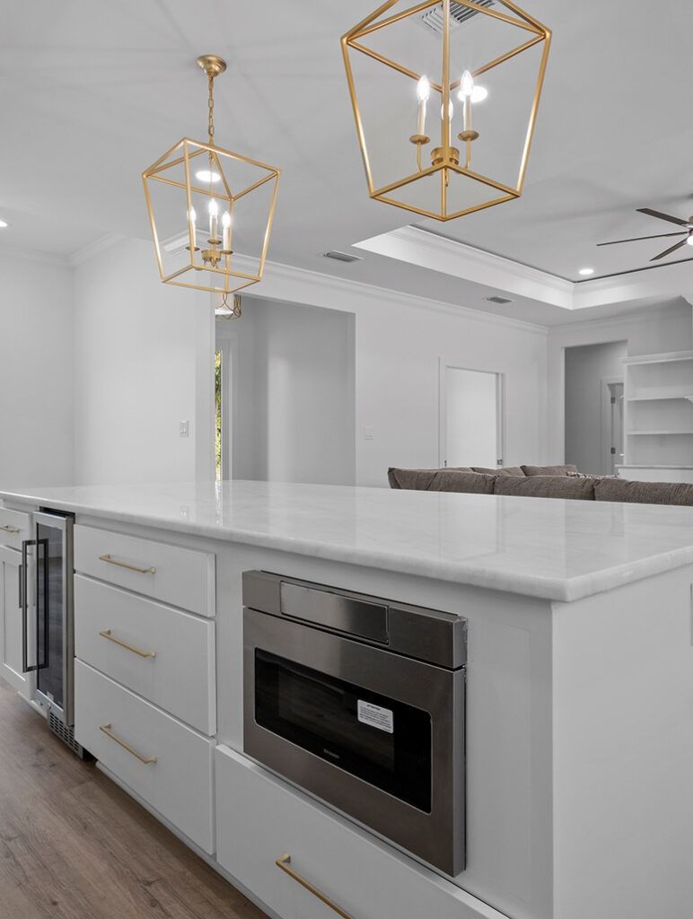 White kitchen island with built-in microwave and refrigerator, gold light fixtures hanging above.