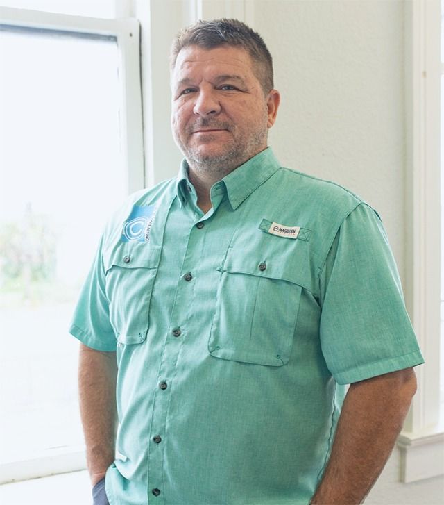 Man in a green shirt smiles, standing near a window.