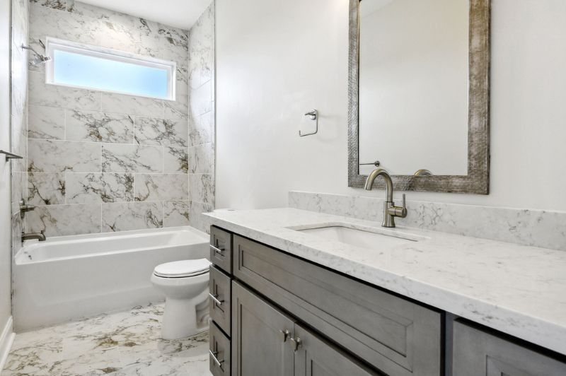 Modern bathroom with gray vanity, white marble tile, and large mirror.