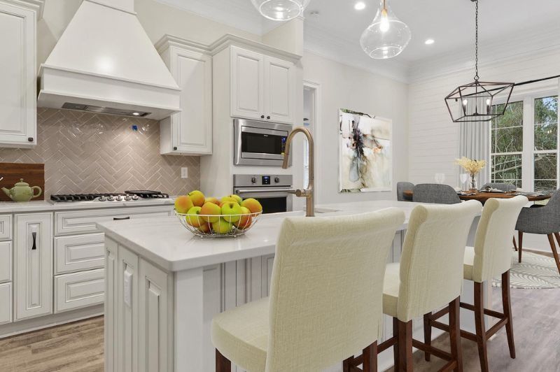White kitchen with island seating, marble countertops, and dining area.