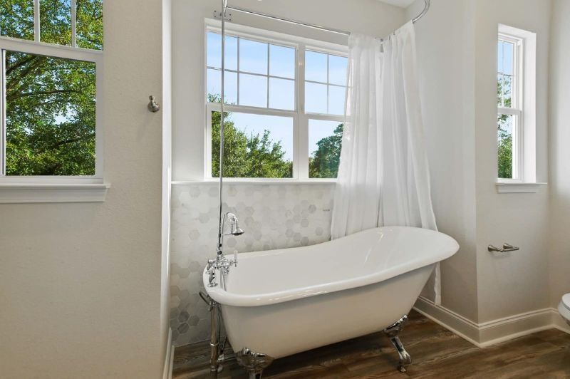 Claw-foot tub in a bathroom with a window, shower curtain, and a view of trees.