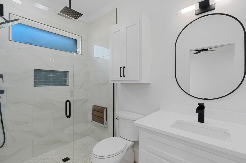 Modern white bathroom with a shower, toilet, vanity, and cabinet; black accents.