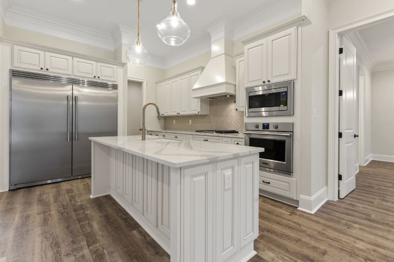 White kitchen with stainless steel appliances, island, and wood-look floors.