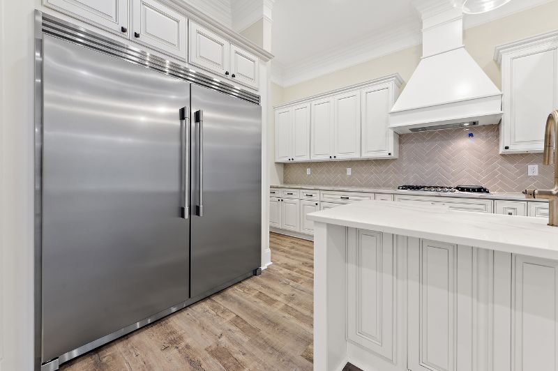 Stainless steel refrigerator and white cabinets in a bright kitchen with wood floors and a white island.