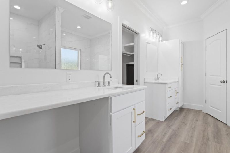 Bright white bathroom with double vanity, neutral flooring, and walk-in closet.
