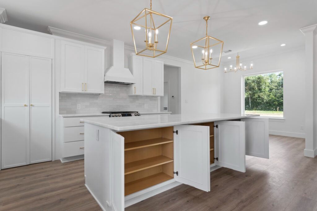 White kitchen with island, open cabinets, gold light fixtures, and light wood floor.