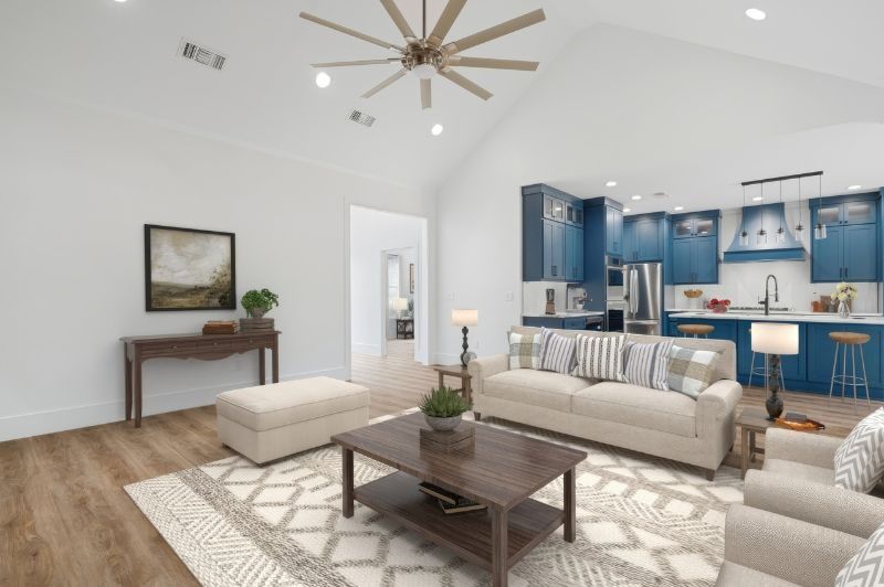 Spacious living room with open kitchen; blue cabinets, neutral furniture, hardwood floors, and vaulted ceiling.