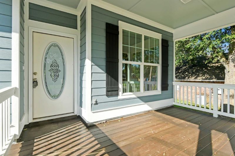 Front porch with blue siding, white door with oval glass, window, and wooden decking.