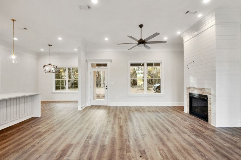 Spacious, bright living room with hardwood floors, fireplace, and large windows overlooking greenery.
