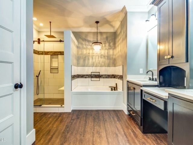 Bathroom with a tub, shower, dark cabinets, and wood-look flooring.