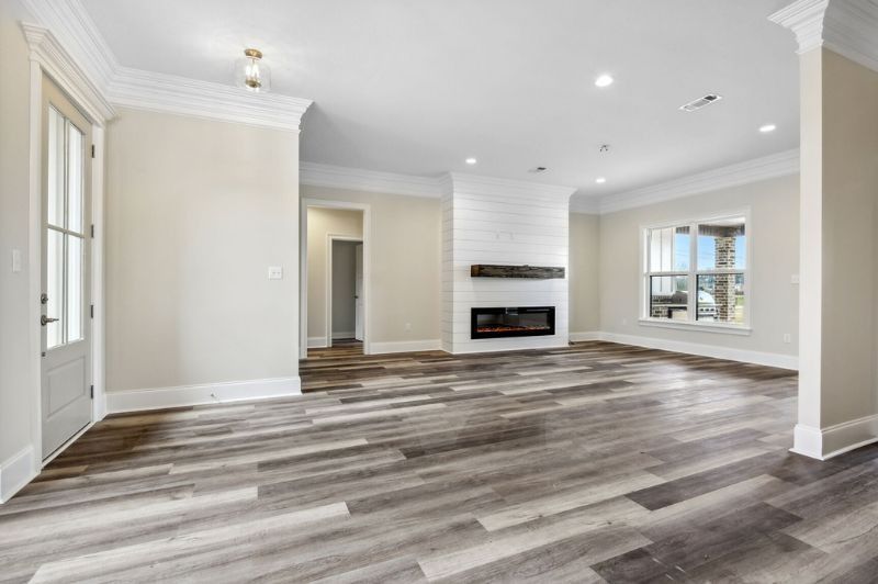 Spacious room with gray wood floors, fireplace, white walls, and a doorway.