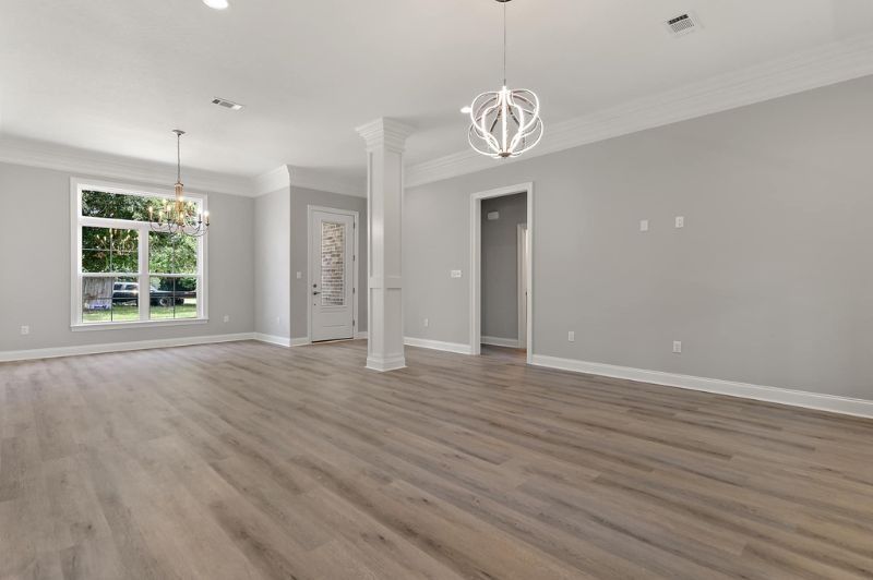 Empty, bright living room with gray walls, light wood floors, and three modern chandeliers.