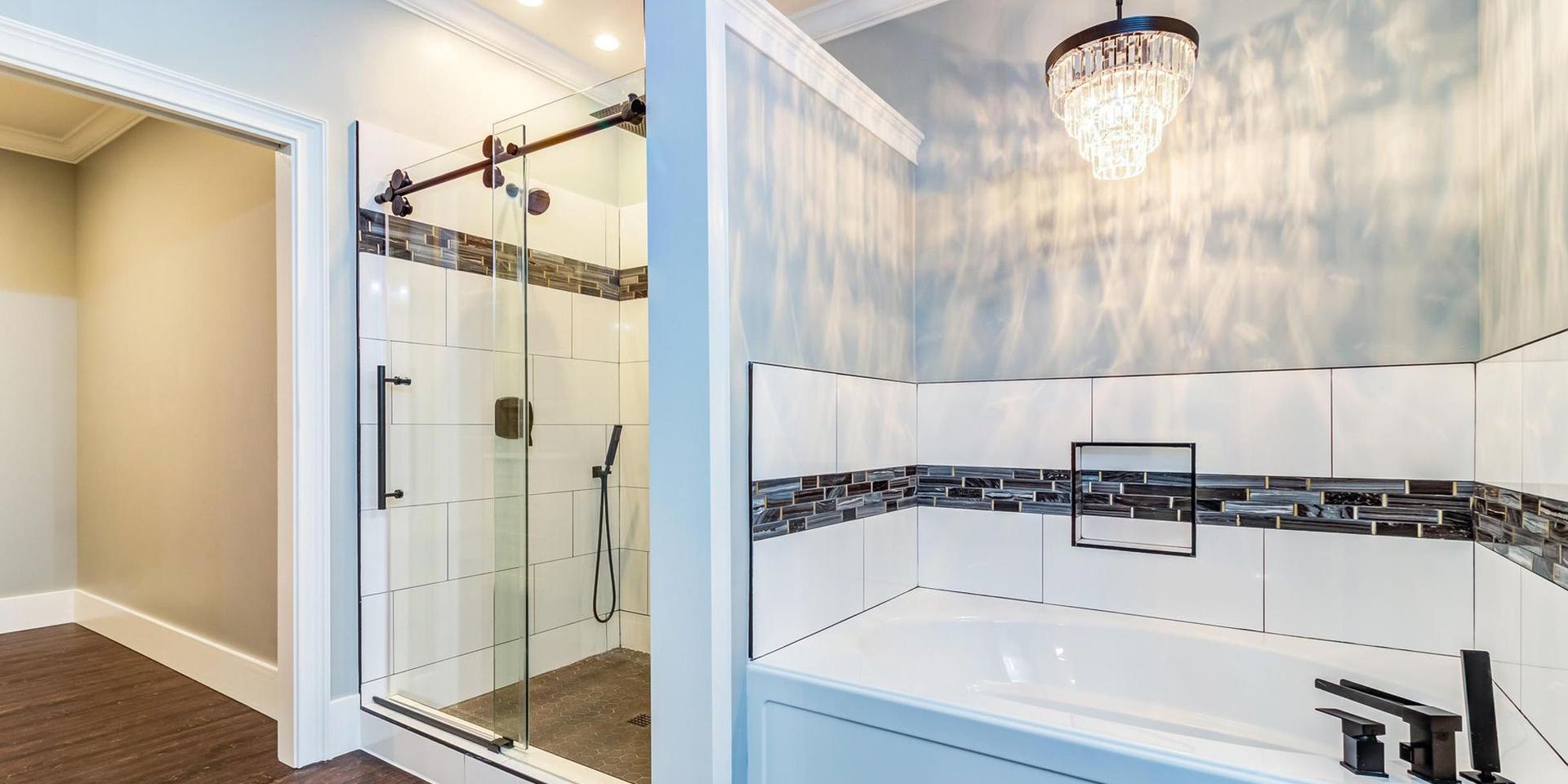 A modern bathroom with a shower and a tub. White tiles, black fixtures, and a crystal chandelier.