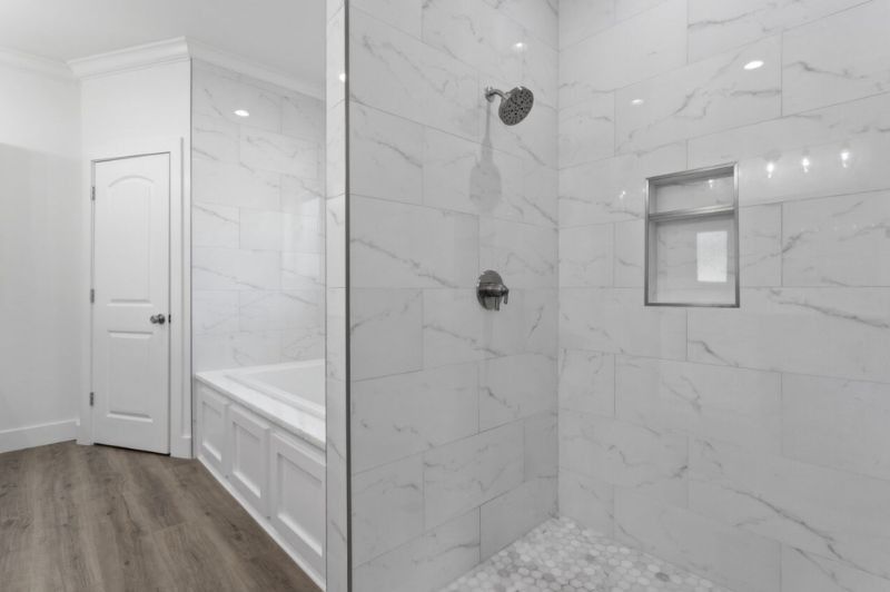 Bathroom with marble tiled shower, tub, and white walls. Gray wood-look floor.
