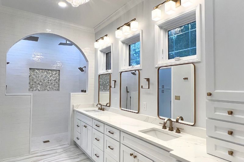 Bright white bathroom with marble countertop, large mirrors, and shower under an arch.