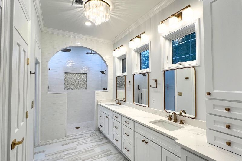 Bright white bathroom with a large shower, double vanity, and gold accents.