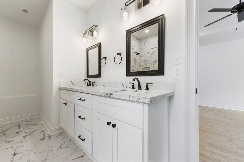 White bathroom with dual vanity, black fixtures, marble countertops and flooring.