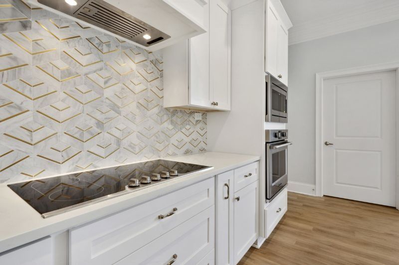 White kitchen with marble tile backsplash, gold accents, built-in appliances, and wooden floors.