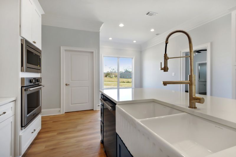 Modern kitchen with white cabinets, blue island, gold faucet, and light-colored hardwood floors.